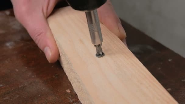 Close-up das mãos de um construtor profissional, ele torce um parafuso em um feixe de madeira com uma broca elétrica. Um artesão profissional dirige um parafuso em um bloco de madeira com uma chave de fenda elétrica. — Vídeo de Stock