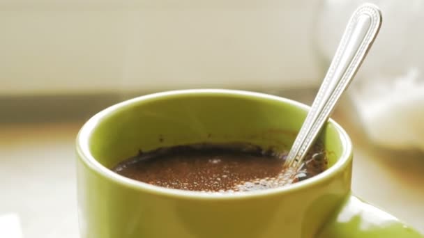Café noir dans une tasse vert clair se tient devant la fenêtre. La vapeur sort d'une tasse de café aromatique. — Video