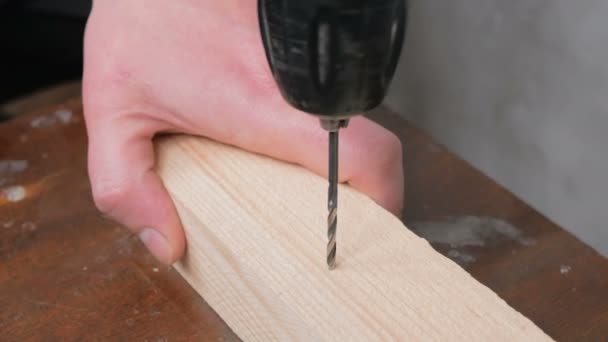 Un artisan professionnel perce un trou avec une perceuse électrique dans un bloc de bois. Gros plan des mains d'un constructeur professionnel, il perce un trou dans une poutre en bois avec une perceuse électrique. — Video