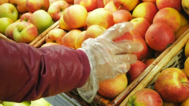 Jovem escolhe maçãs orgânicas maduras no supermercado. Mulher atraente jovem pega maçãs orgânicas maduras no supermercado durante a quarentena. Close-up de uma mão de mulheres jovens em um protetor — Vídeo de Stock