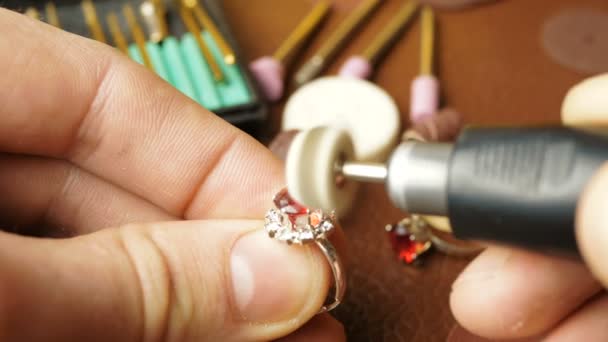 Le bijoutier est engagé dans la découpe d'une pierre précieuse sur une bague en or.Un bijoutier professionnel polit une gemme rouge sur une bague en or à l'aide d'un outil spécial. — Video