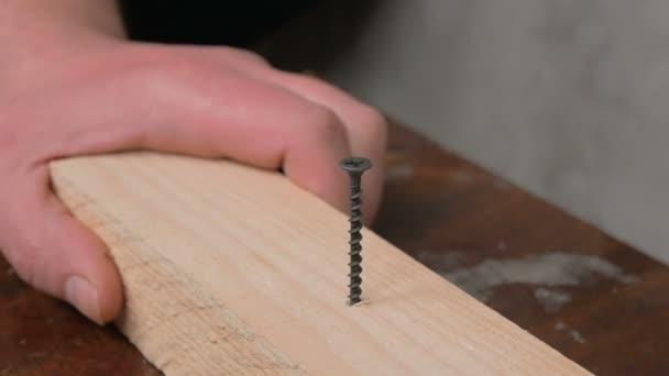 Close-up das mãos de um construtor profissional, ele torce um parafuso em um feixe de madeira com uma broca elétrica. Um artesão profissional dirige um parafuso em um bloco de madeira com uma chave de fenda elétrica. — Vídeo de Stock