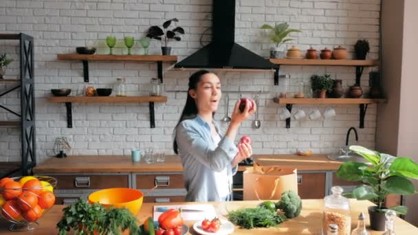 Young Beautiful Woman lays out the products from the package on the table. A beautiful young woman in a good mood is sorting vegetables from a bag and putting them on the kitchen table. — 图库视频影像