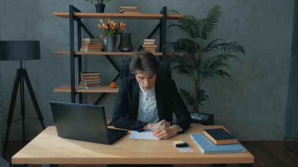 Νέος όμορφος επιχειρηματίας συμπληρώνει οικονομικές καταστάσεις, ενώ κάθεται στο γραφείο του.Νέοι επιχειρηματίες προοπτική εργάζεται ενεργά, ενώ κάθεται στο τραπέζι στο γραφείο. Νέα ελκυστική — Αρχείο Βίντεο