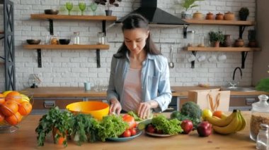 Mutlu genç ev hanımı mutfağında sebze salatası hazırlıyor. Keyfi yerinde güzel genç bir kadın salata için marul yaprakları kesiyor. Genç ve güzel bir kadın salata için sebze kesip içine koyuyor.