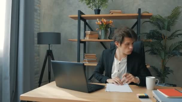 Молодой привлекательный бизнесмен заполняет финансовые отчеты, сидя в своем офисе. Молодой перспективный бизнесмен активно работает, сидя за столом в офисе. Молодые привлекательные — стоковое видео