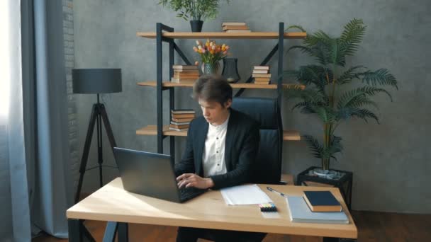 Νέοι επιχειρηματίες προοπτική εργάζεται ενεργά, ενώ κάθεται στο τραπέζι στο γραφείο.Νέοι ελκυστική επιχειρηματίας που εργάζονται σε ένα φορητό υπολογιστή στο γραφείο του. Νέος όμορφος επιχειρηματίας γράφει μια οικονομική — Αρχείο Βίντεο