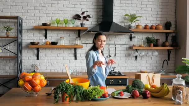 A happy young housewife in a good mood sings funny into a metal spoon and dances merrily in her kitchen. An attractive young woman sings and dances while preparing dinner for her loving boyfriend — Stock Video