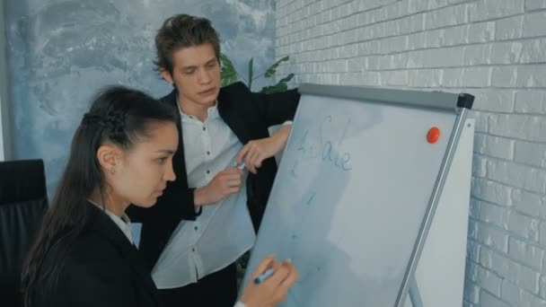 Młoda bizneswoman i obiecujący biznesmen opracowują nową koncepcję dla swojej marki, narysować plan z markerem na tablicy. Młody chłopak i piękna atrakcyjna dziewczyna dyskutują o — Wideo stockowe