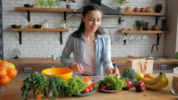 Beautiful young woman in a good mood cuts lettuce leaves for salad. Young beautiful woman cuts vegetables for salad and puts them in a bowl. Happy young housewife prepares vegetable salad in her — Stock Video