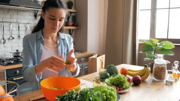 Όμορφη νεαρή γυναίκα με καλή διάθεση κόβει φύλλα μαρουλιού για σαλάτα. Ευτυχισμένη νεαρή νοικοκυρά ετοιμάζει σαλάτα λαχανικών στην κουζίνα της. — Αρχείο Βίντεο