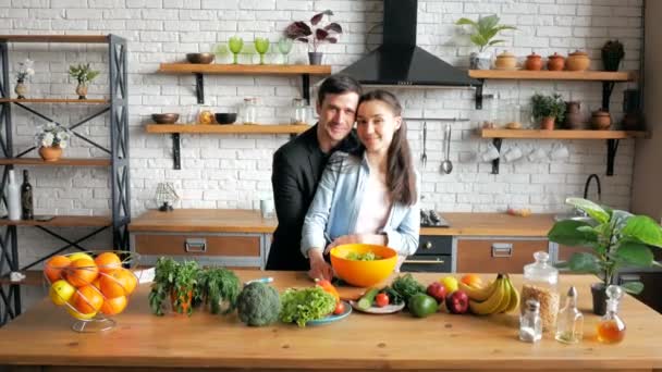 Un joven y atractivo hombre de negocios regresa a casa después del trabajo, besa y abraza a su esposa en la cocina de su apartamento.Una joven ama de casa feliz invita a su marido a cenar en su cocina. Joven hermosa — Vídeos de Stock