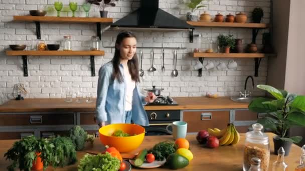 Feliz ama de casa joven en un buen estado de ánimo disfruta de café recién hecho mientras está sentado en una mesa en la cocina. Una joven mujer despreocupada en un ambiente romántico bebe té de una taza azul en la cocina de su — Vídeos de Stock