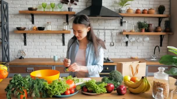 Felice giovane casalinga prepara insalata di verdure nella sua cucina. Giovane bella donna taglia le verdure per l'insalata e li mette in una ciotola. — Video Stock