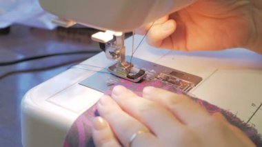 İlgili genç ev hanımı dikiş makinesi kullanarak elbise dikiyor. Genç ve çekici bir moda tasarımcısının ellerini yakın plan çekimde dikiş makinesine yeni bir elbise modeli dikiyor. Şunun yakın çekimi: