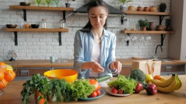 Keyfi yerinde güzel bir genç kadın salata için salatalık keser. Mutlu genç ev hanımı mutfağında sebze salatası hazırlıyor. Genç ve güzel bir kadın salata için sebze kesip içine koyuyor.