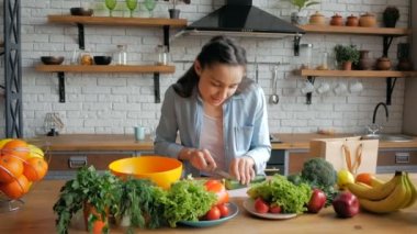 Keyfi yerinde güzel bir genç kadın salata için salatalık keser. Mutlu genç ev hanımı mutfağında sebze salatası hazırlıyor. Genç ve güzel bir kadın salata için sebze kesip içine koyuyor.