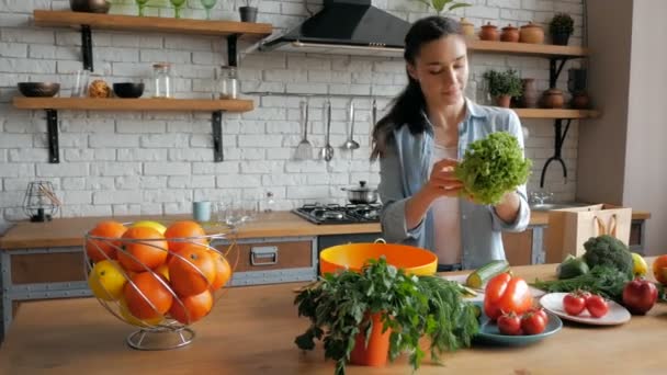 Bella giovane donna di buon umore taglia le foglie di lattuga per l'insalata. Felice giovane casalinga prepara insalata di verdure nella sua cucina. — Video Stock