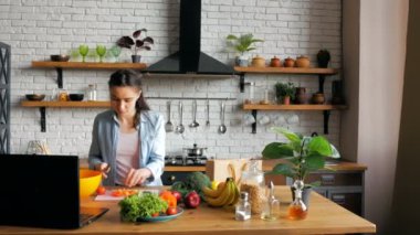 Neşeli genç ev hanımı, görüntülü konuşma dersinden sonra salata hazırlar. Genç ve güzel bir kadın, internette bir tarifi takip ediyor, salata için sebze kesiyor ve bir kaseye koyuyor..