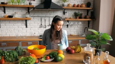 Romantik bir ruh hali içinde kaygısız genç bir kadın dairesinin mutfağındaki mavi bardaktan çay içer. Mutlu genç ev hanımı keyifli bir ruh hali içinde masada otururken yeni demlenmiş kahvenin tadını çıkarıyor.