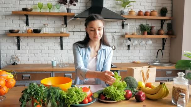 Jovem dona de casa feliz prepara salada de legumes em sua cozinha.Jovem bonita em um bom humor corta folhas de alface para salada. — Vídeo de Stock