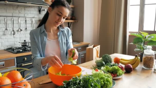 기분좋은 아가씨가 샐러드에 양상추 잎을 자르네요. 젊고 아름다운 여자는 샐러드를 만들기 위해 야채를 썰어서 그릇에 담습니다. 행복 한 젊은 주부 가 속에 야채 샐러드를 준비 한다 — 비디오
