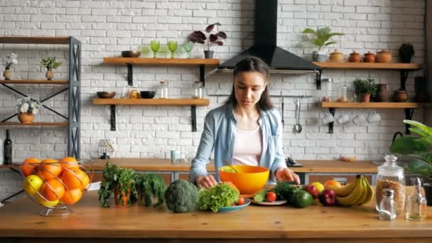 Giovane bella donna insieme al suo amato marito preparare un'insalata di verdure nella cucina del loro appartamento.Una giovane casalinga felice tratta il marito a cena nella sua cucina. — Video Stock