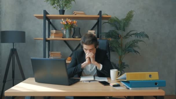 Mladý atraktivní podnikatel pracuje na notebooku po dlouhou dobu a unaveně si tře oči, zatímco sedí u stolu ve své kanceláři.Mladý pohledný podnikatel píše finanční zprávu na notebook a — Stock video