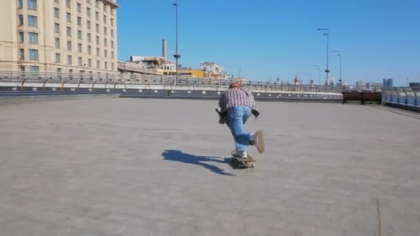 Un ragazzo giovane millenario che guida uno skateboard spensierato in città. Un ragazzo giovane e attraente sta cavalcando uno skateboard. Uno skateboarder professionista guida uno skateboard lungo l'argine della città. — Video Stock