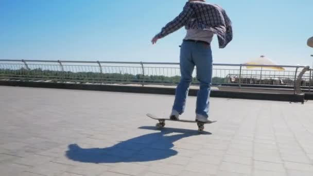 Um cara jovem millennial que monta um skate despreocupado na cidade.Jovem cara atraente está montando um skate. Um skatista profissional monta um skate ao longo do dique da cidade. O — Vídeo de Stock