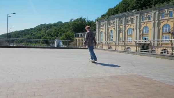 Um jovem milenar que monta um skate despreocupado na cidade. Jovem atraente está montando um skate. Um skatista profissional monta um skate ao longo do dique da cidade. O — Vídeo de Stock