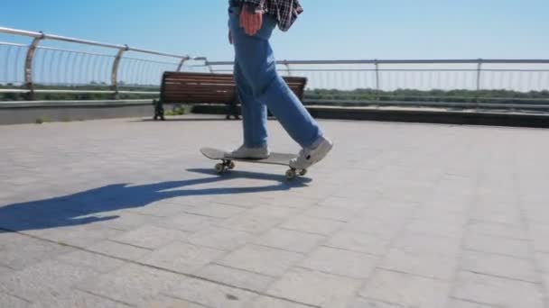 Jovem atraente está montando um skate. Um skatista profissional monta um skate ao longo do dique da cidade. Um skatista profissional monta um skate ao longo da orla da cidade e — Vídeo de Stock