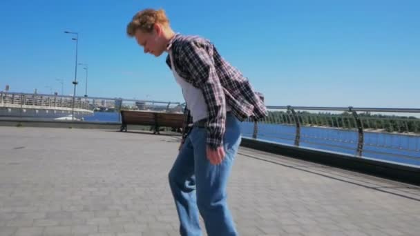 Um cara jovem faz um kickflip enquanto monta um skateboard.Young cara atraente está montando um skate. Um skatista profissional monta um skate ao longo do dique da cidade. O profissional — Vídeo de Stock