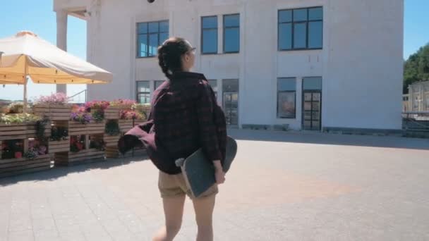 Молодая красивая женщина, идущая по пешеходной набережной с скейтбордом в руках. — стоковое видео
