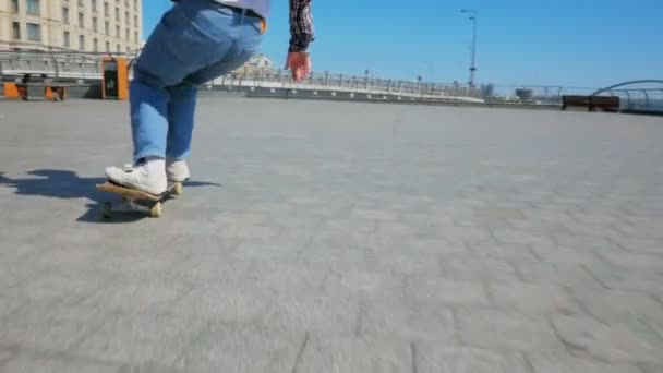 Um cara jovem millennial que monta um skate despreocupado na cidade.Jovem cara atraente está montando um skate. Um skatista profissional monta um skate ao longo da orla da cidade e faz — Vídeo de Stock