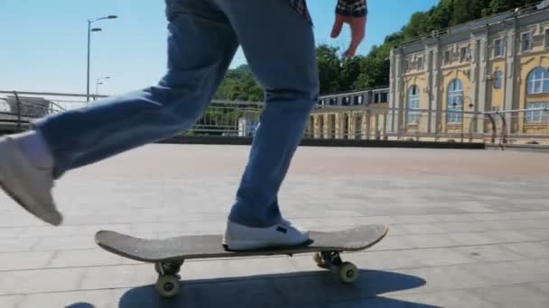 Jovem atraente está montando um skate. Um skatista profissional monta um skate ao longo do dique da cidade. O skatista profissional executa truques para melhorar suas habilidades. Um jovem rapaz. — Vídeo de Stock