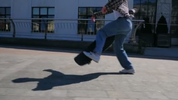 O skatista profissional executa truques para melhorar suas habilidades.Jovem cara atraente está montando um skate. Um skatista profissional monta um skate ao longo do dique da cidade. Um jovem — Vídeo de Stock