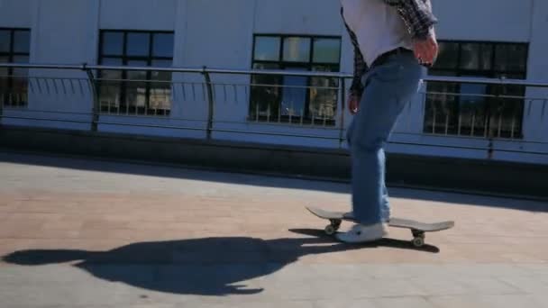 Молодой привлекательный парень едет на скейтборде. Профессиональный скейтбордист катается на скейтборде вдоль береговой линии города и делает экстремальные трюки. Молодой парень тысячелетия, который ездит на скейтборде беззаботно — стоковое видео