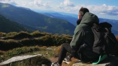 Genç ve çekici bir yürüyüşçü uçurumun tepesinde oturur ve dağ manzarasının muhteşem manzarasının tadını çıkarır..