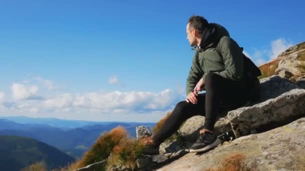 Ung kille resenär njuter av utsikten över bergskedjan medan du sitter på toppen av klippan. — Stockvideo