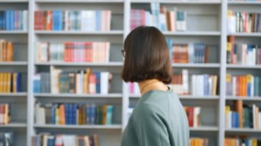 Genç bir milenyum kadını, kütüphanenin arka planında dururken kameraya bakıp gülümsüyor. Arka planda genç bir kız öğrencinin yakın plan portresi