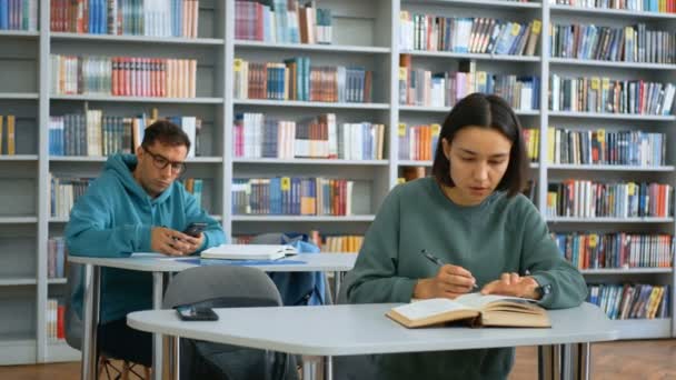 Κοντινό πλάνο πορτρέτο ενός νεαρού ελκυστικού φοιτητή και μιας νεαρής χαρούμενης φοιτήτριας, ψάχνουν για τις απαραίτητες πληροφορίες σε ένα βιβλίο ενώ ετοιμάζονται για ένα μάθημα. — Αρχείο Βίντεο