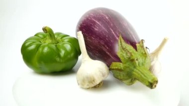 Patlıcan, dolmalık biber, domates, sarımsak ve bıldırcın yumurtası bir tabakta yatar ve beyaz arka planda döner. Sağlıklı gıda konsepti.