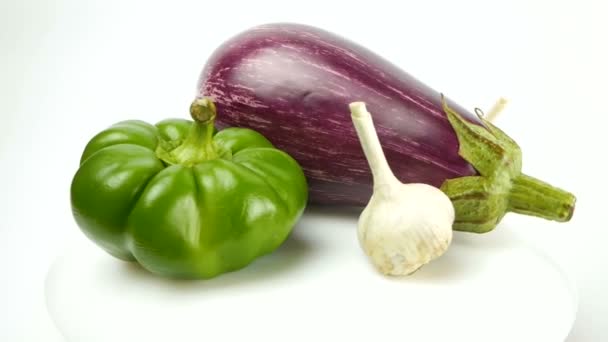 Eggplant, bell pepper, tomato, garlic and quail egg lie on a plate and rotate on a white background. Healthy food concept. Fresh juicy organic vegetables rotate on a white plate. — Stock Video