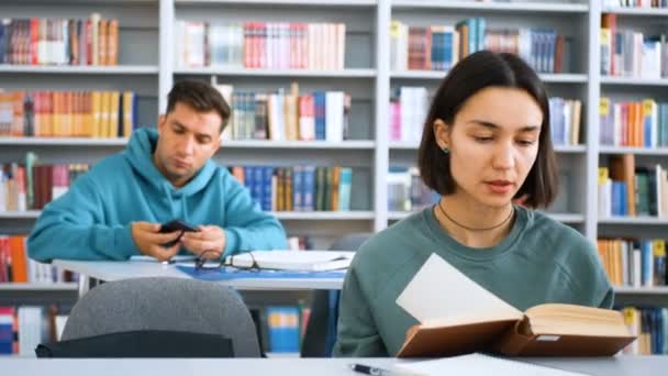 Närbild porträtt av en ung attraktiv student kille och en ung glad kvinnlig student, de letar efter nödvändig information i en bok. Utbildningsidé. — Stockvideo