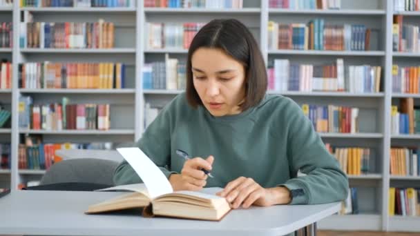 Detailní záběr portrét mladé veselé studentky, hledá potřebné informace v knize a píše do zápisníku, připravuje se na lekci. Koncept vzdělávání. — Stock video