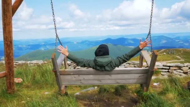 An attractive young traveler rides a large swing, arms outstretched, at the top of a cliff and enjoys the beautiful view. Young attractive hiker is riding a swing on the top of the mountain and — Stock Video