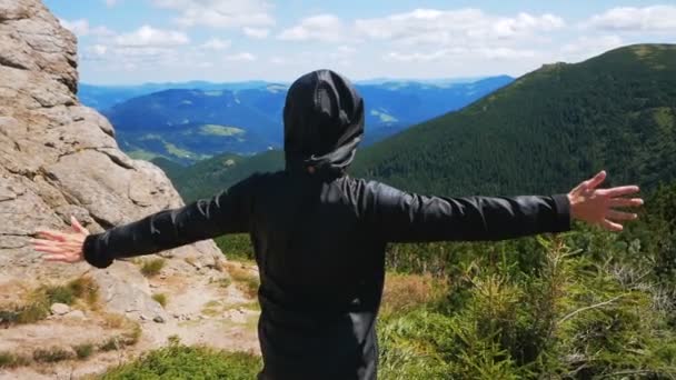 Na vrcholu útesu stojí mladá cestovatelka a dívá se na horskou krajinu. Mladá atraktivní žena cestovatel stojí na vrcholu hory a dívá se do dálky na — Stock video