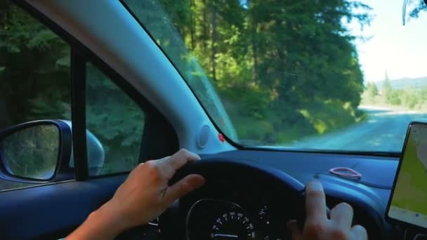 Close-up van de handen van een jonge vrouw liggen op het stuur van een auto, ze rijdt langs een bergweg, het controleren van de kaart op de navigator in haar smartphone. — Stockvideo