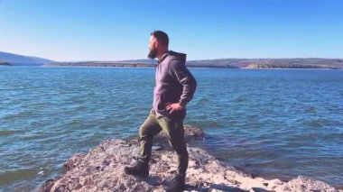 Genç ve çekici bir turist bir dağ gölünün kayalık kıyısında duruyor ve manzaranın tadını çıkarıyor. Yüksek kalite 4k görüntü